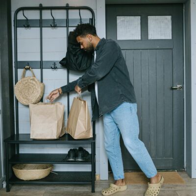 Man arranges paper shopping bags in a stylish entryway, combining fashion and home organization.
